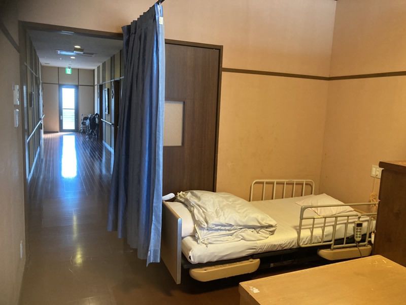 寝具付きのベッドが置かれ小さな家具が置かれた居室。ブルーのカーテンで仕切ることができる。