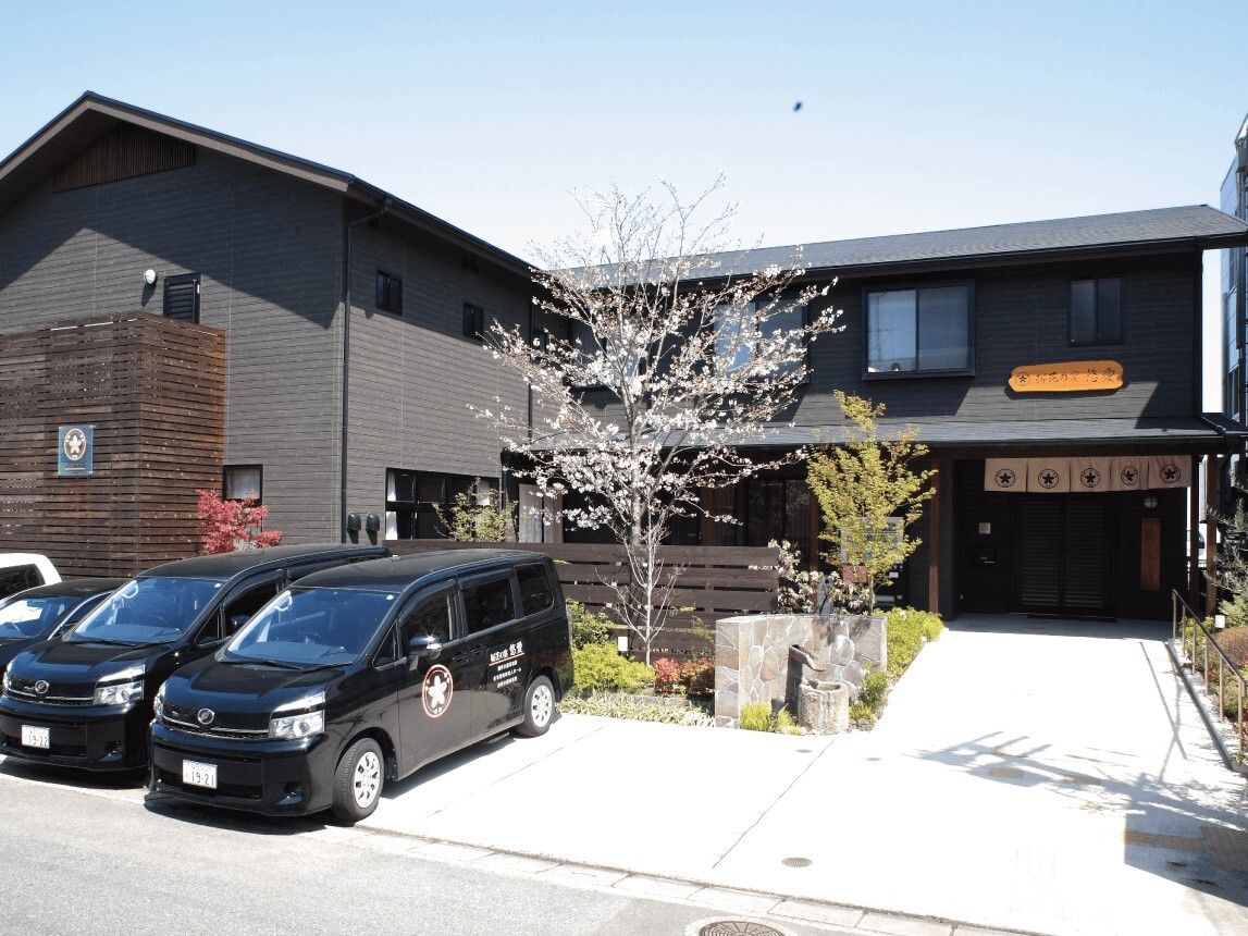 ダークグレーの２階建ての建物はエル字型で玄関からは緩やかなスロープが続いていて、草木も植えられている。