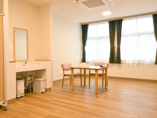 レースカーテンとカーテンが付いた大きな窓がある共有スペースにはテーブルセットが置かれ、洗面所がある。