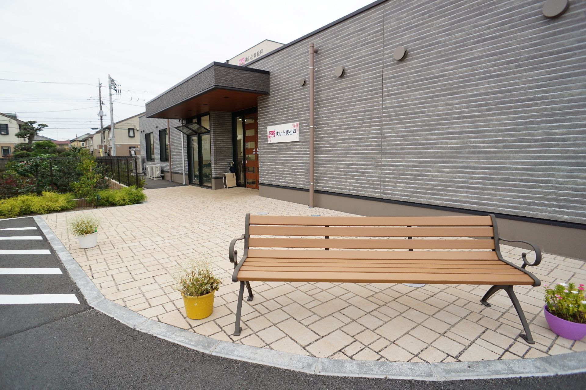 カーディガンを着た車いすの高齢女性とエプロンを付けた女性スタッフが屋外で笑顔で散歩を楽しんでいる。