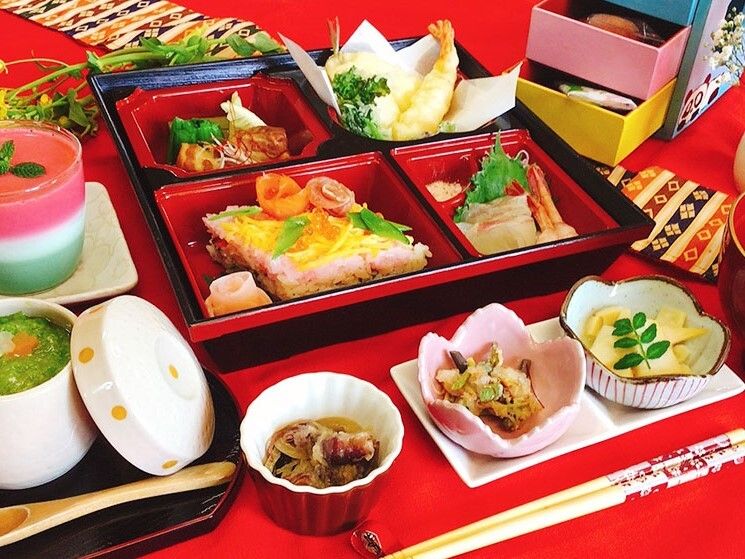寿司や天ぷら、煮物が詰められた松花堂弁当風の食事。前菜盛りやデザート、茶碗蒸しなども並んでいる。