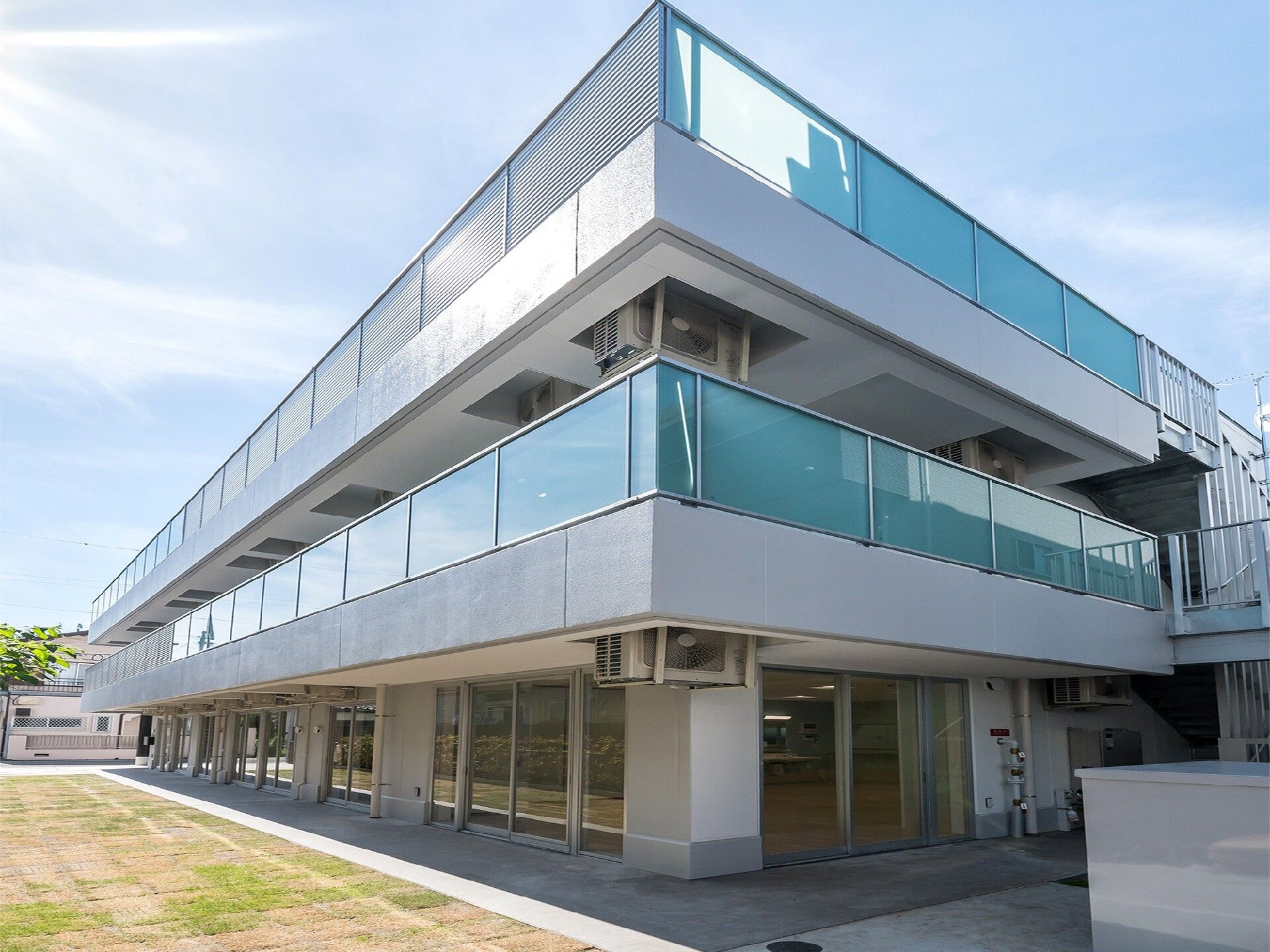 各フロアにベランダが付いた３階建ての建物の玄関には屋根があり、子連れの家族やスタッフに付き添われた車いすの高齢女性がいる。