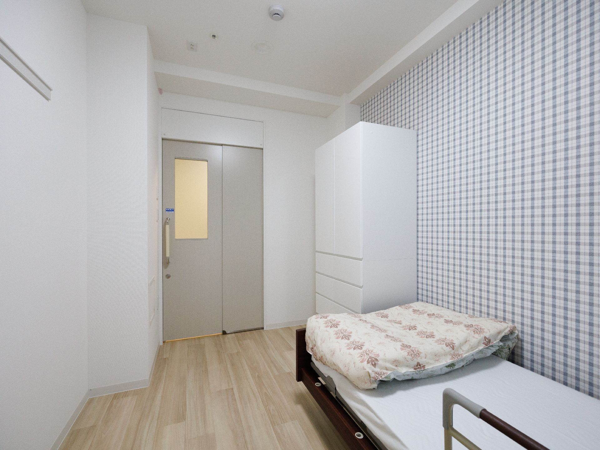 白い壁際に収納棚と白いマットレスの敷かれたベッドが配置された部屋