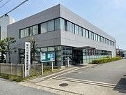 グレーの２階建ての建物は日当たり良好で館銘板が立ち、周りには草木が植えられている。