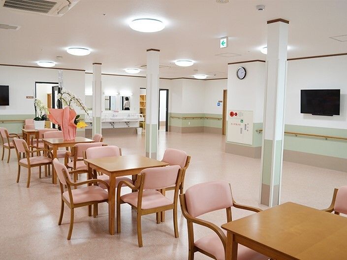 ピンクのいすが設置された４人掛けのダイニングテーブルが複数置かれている明るい雰囲気の食堂。