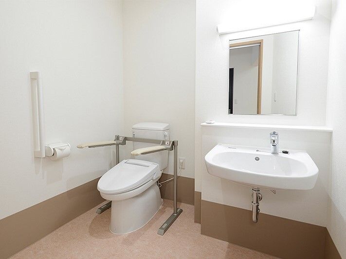 右側には鏡が付いた洗面所があり、左側には壁と便座に手すりが付いたトイレがある。