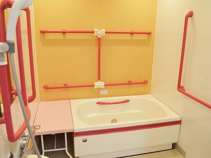 赤い手すりがたくさん設置された一人用の浴槽が設置された浴室。浴槽脇にはベンチもある。