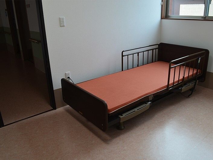 小さな窓が付いたフラットフロアの居室にはオレンジのマットレスが付いたベッドがある。