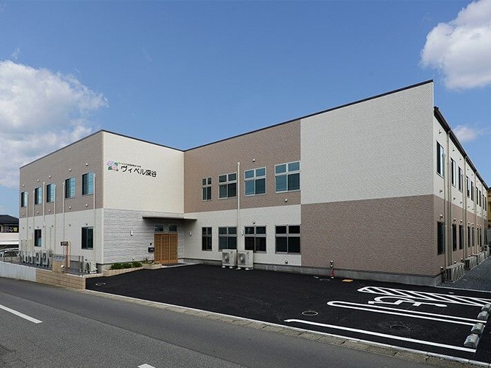 白とベージュの2階建ての建物の外壁には住宅名が書かれ、玄関には車寄せが付き、敷地内には駐車場がある。