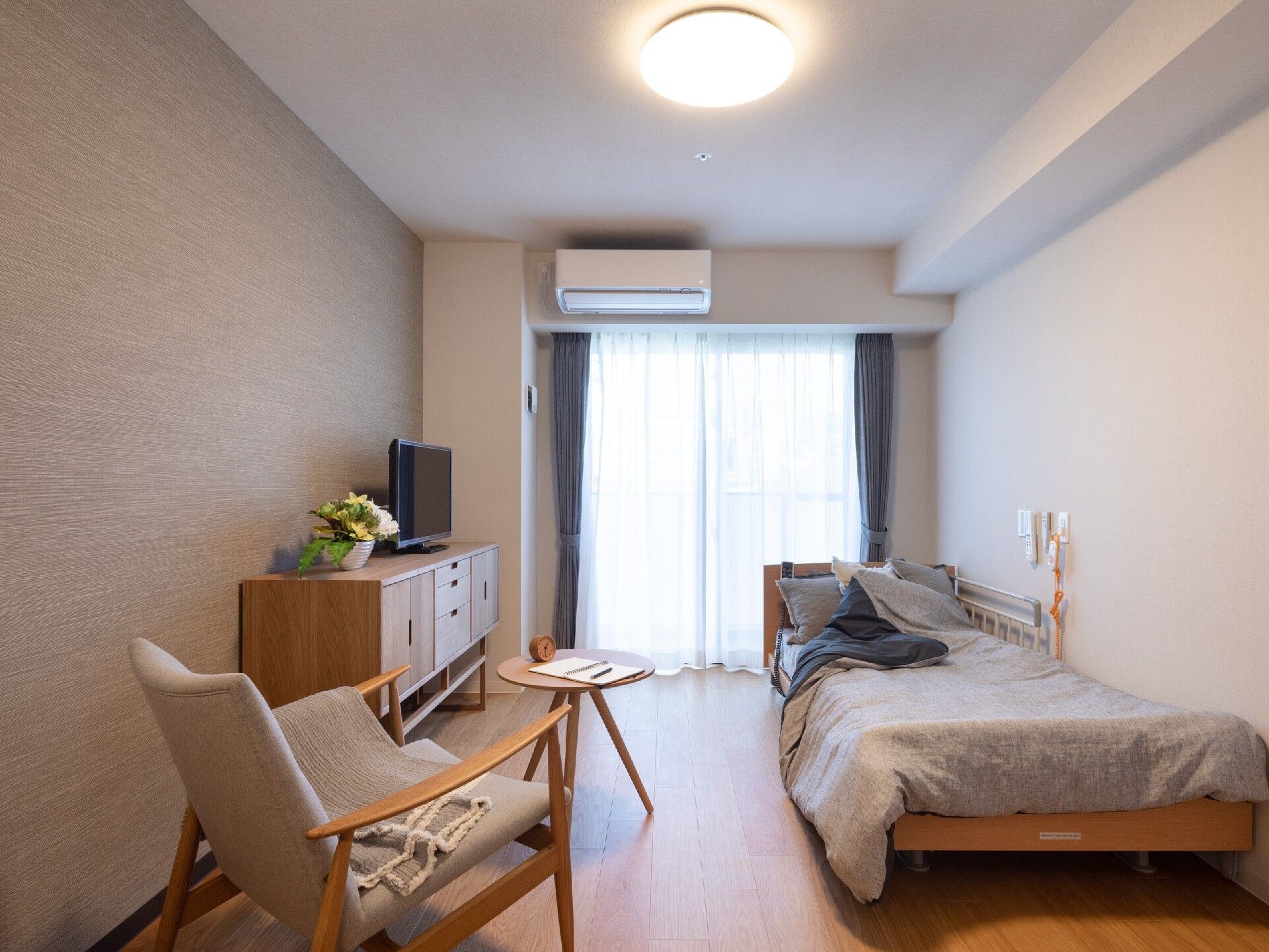 緑の多い屋外にあるパラソル付きのテーブルセットで笑顔で過ごしている高齢の男女。スタッフが話しかけている。