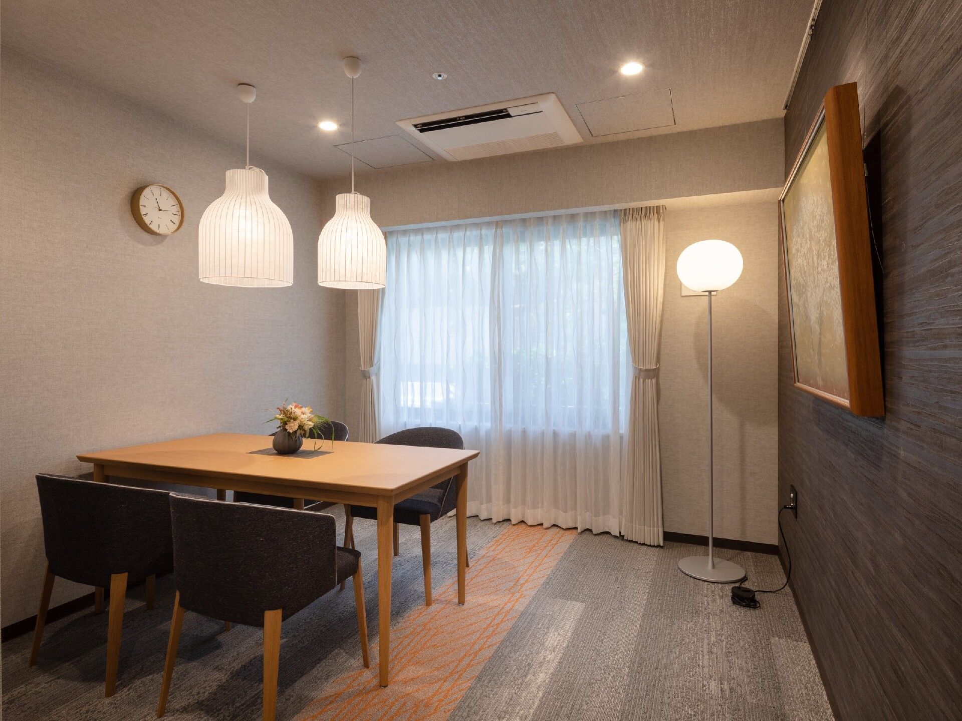 ペンダントライトが設置され、4人掛けのテーブルセットが置かれた部屋には絵画が飾られている。