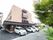 目の前に車が止まっているベージュの外観で３階建ての建物