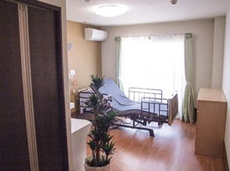 介護ベッドが置かれたフローリングの部屋には観葉植物が置かれ、エアコンが設置されている。