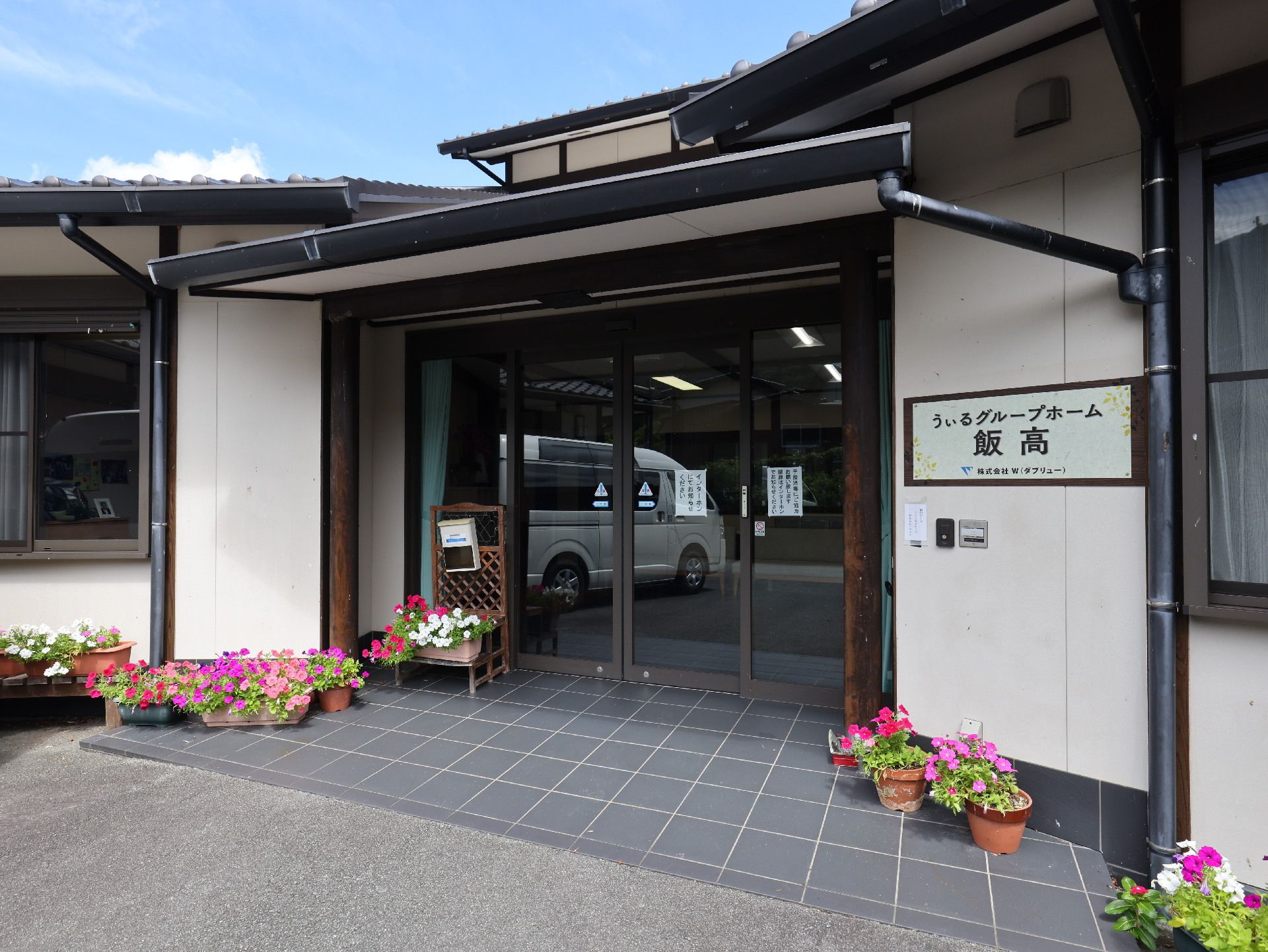 原っぱのような場所を笑顔で歩いているジャケットを着た高齢女性と付き添いの若い女性スタッフ。