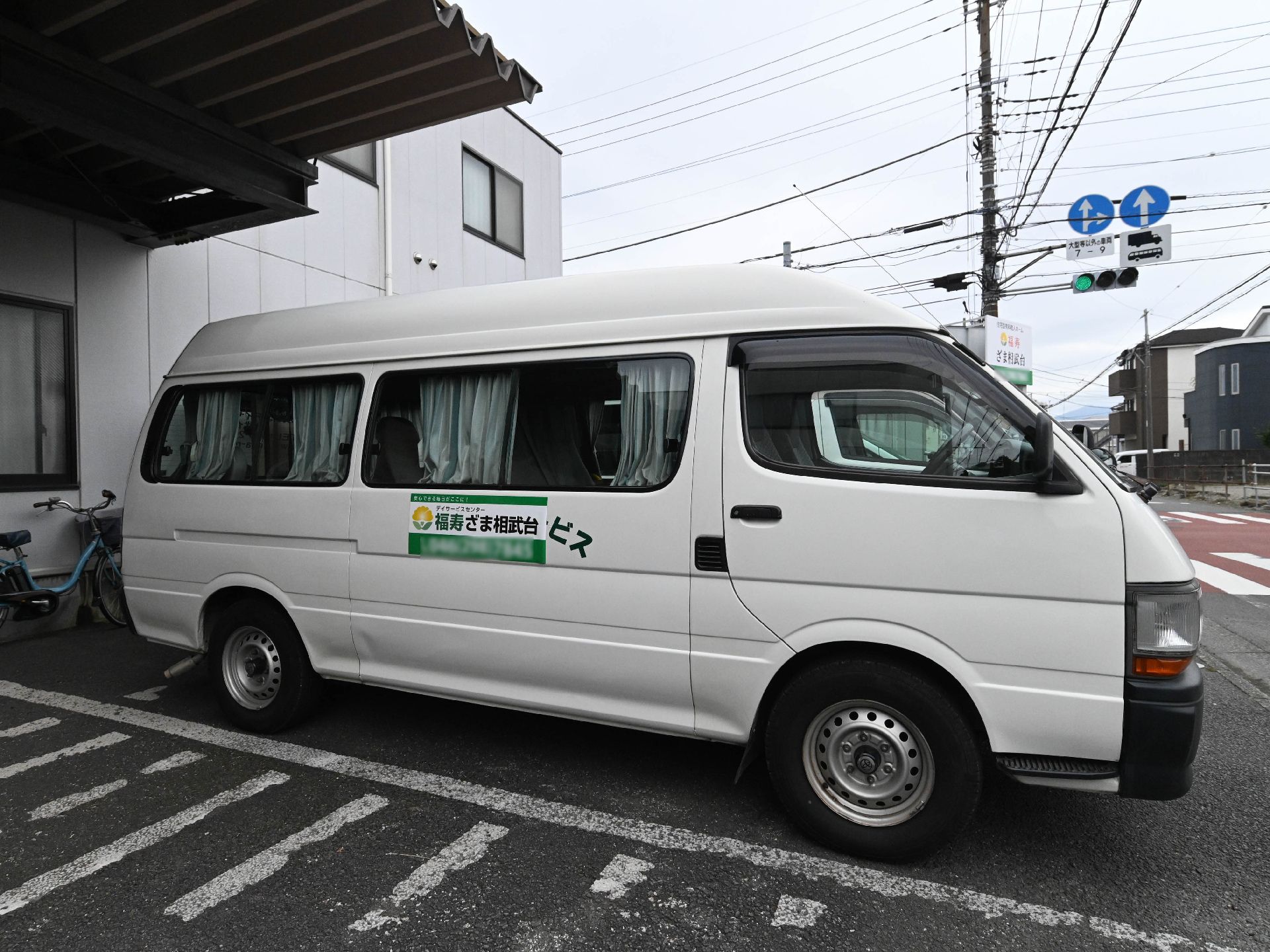 眼鏡をかけた高齢男性が福祉車両から下りようとしているところをサポートしている若いスタッフ。