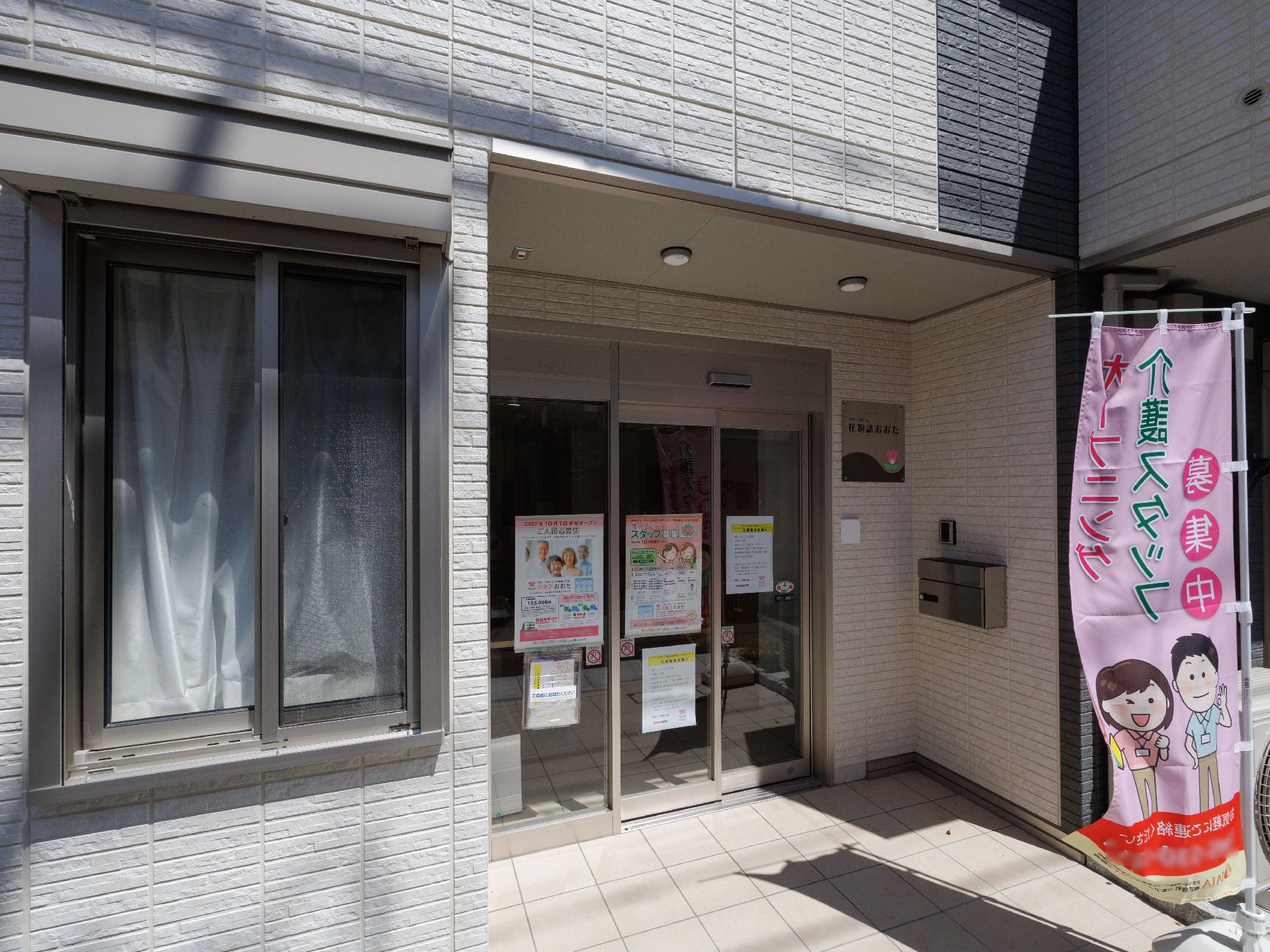 水の入ったコップを持ったエプロンを付けた女性スタッフが薬を飲もうとしている高齢女性のそばにいる。