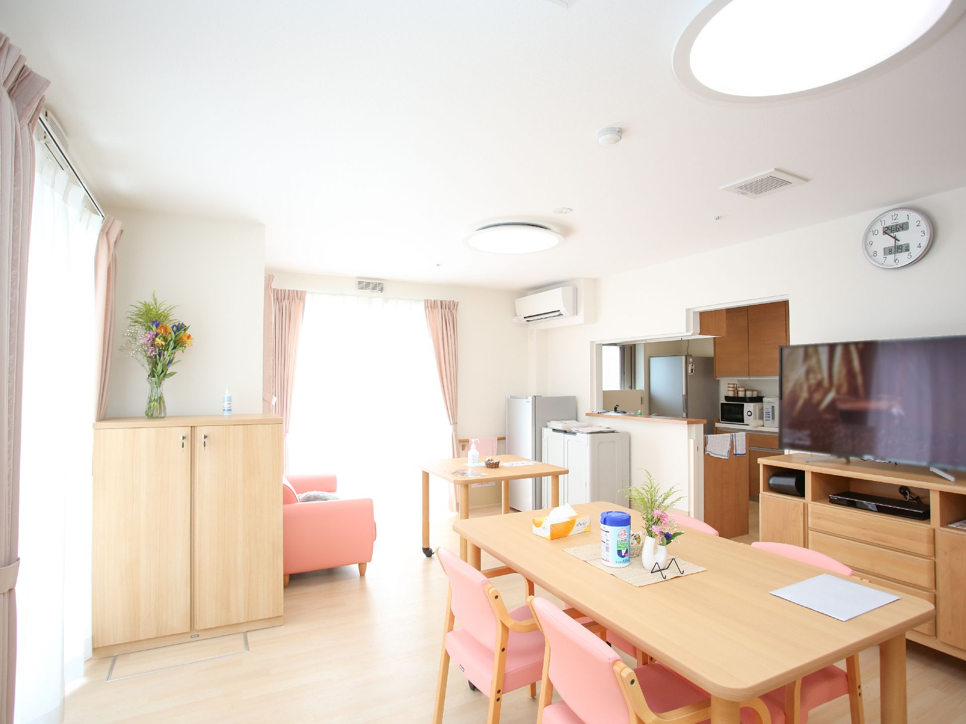 木製の机とピンクのクッションが付いた椅子の置かれた白い壁の部屋