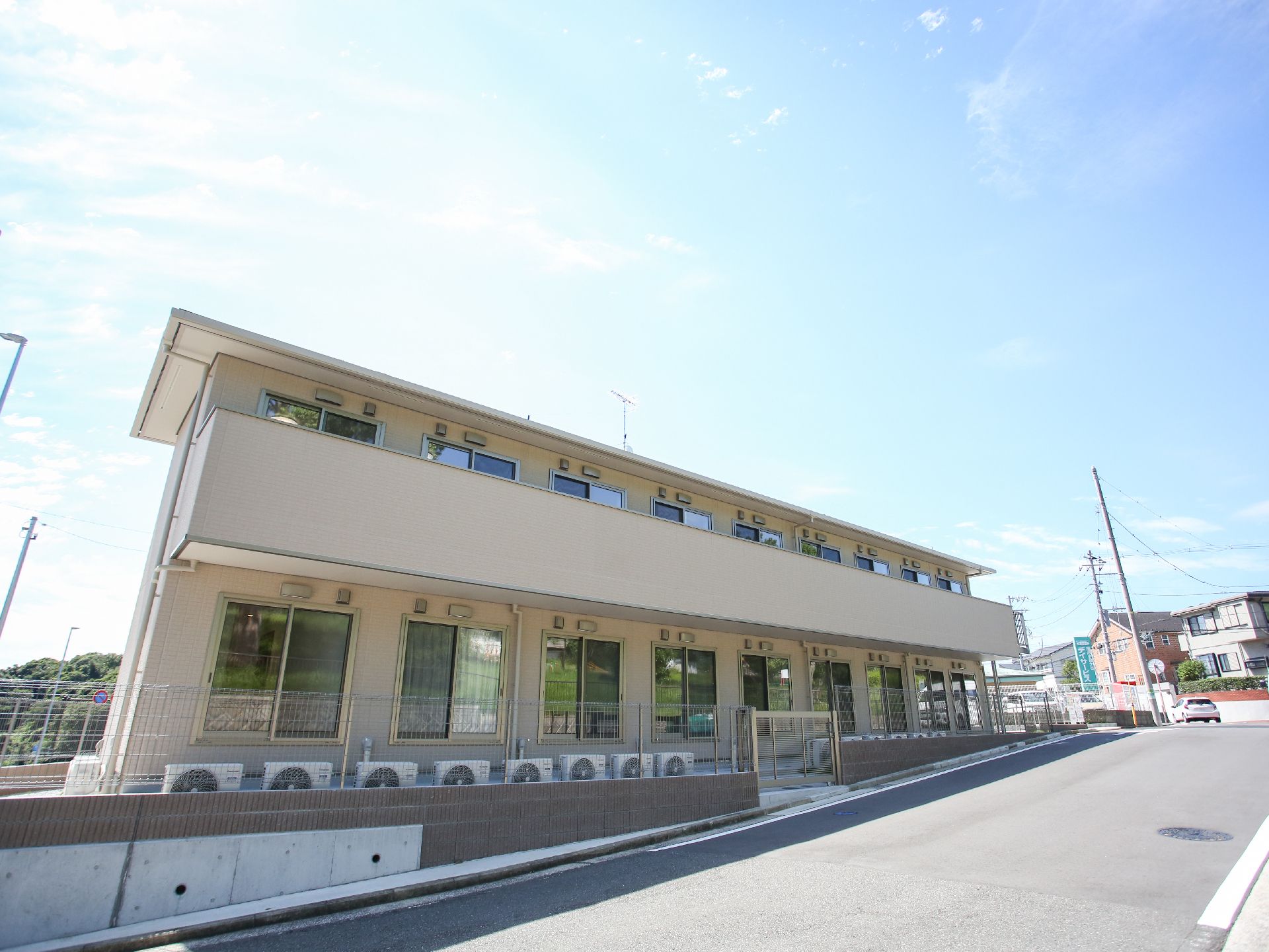アスファルトに隣接したベージュの外観で２階建ての建物