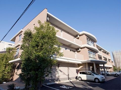 青空を背景にやさしい色合いの建物が建っている。建物の前に駐車場を完備しており、軽自動車専用の駐車場もある。