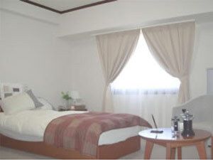 寝具付きのベッドやテーブルが置かれた居室にはレースカーテンとカーテンが付いた窓がある。