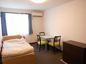 エアコンが付いた部屋には寝具付きのベッドや大きな窓があり、レースカーテンとカーテンが付いている。