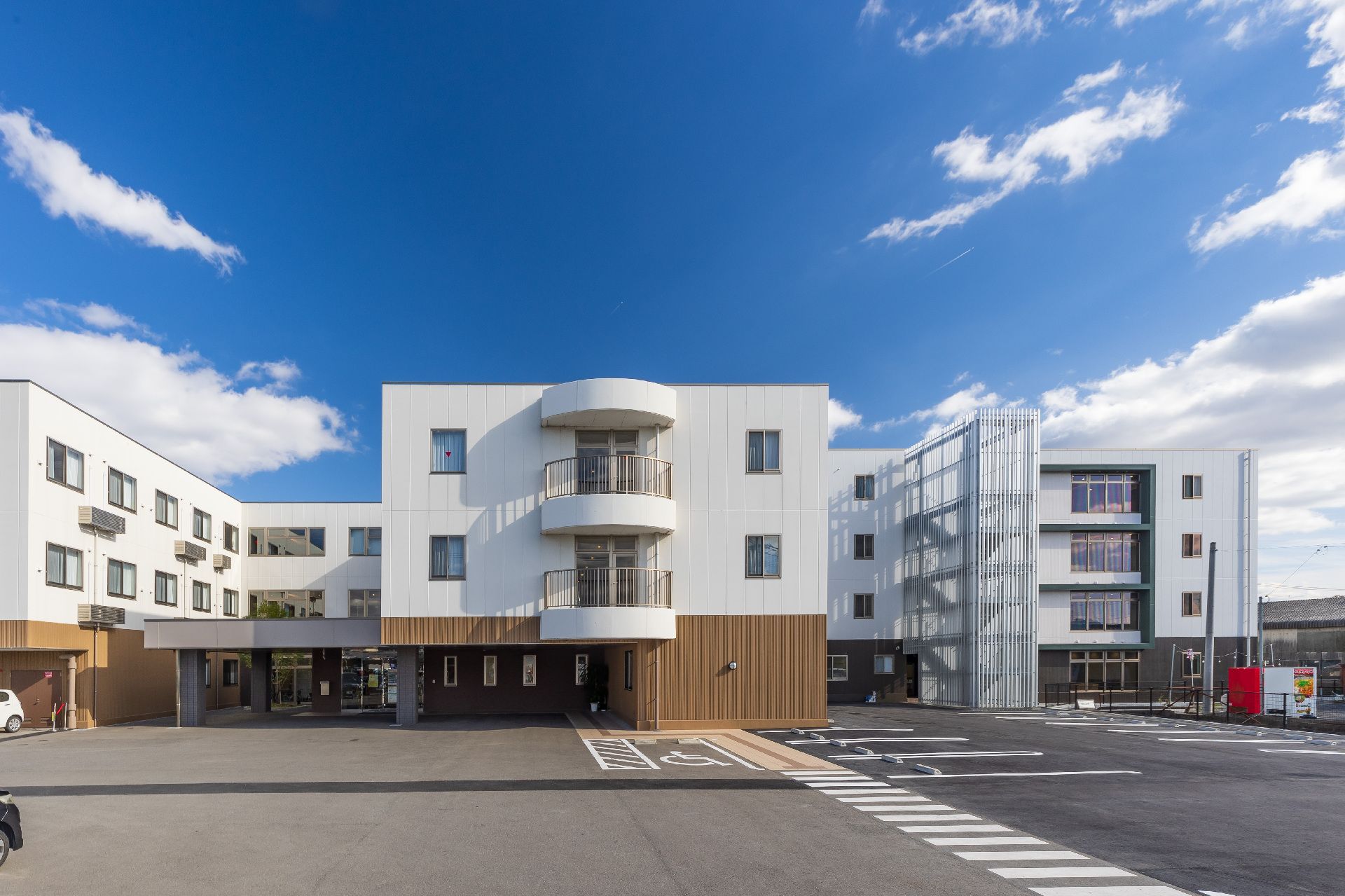 白とグレー、赤の4階建ての建物が右側にあり、左側には白とベージュの3階建ての建物がある。