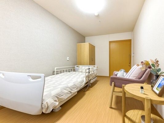 水の入ったコップを持ったエプロンを付けた女性スタッフが薬を飲もうとしている高齢女性のそばで待っている。