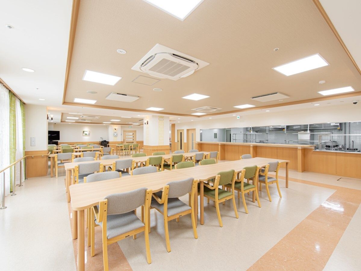厨房がすぐそばにある食堂。椅子がセットされた長方形のテーブルセットが複数あり、テレビもある。
