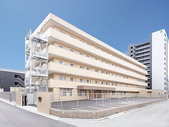 各フロアにベランダがあり、屋外階段も付いている5階建てのベージュ系の外壁の建物。