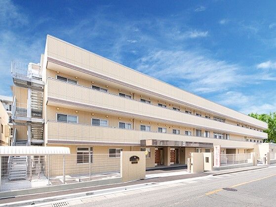 ベージュ系の３階建ての建物は横に長く、各フロアにベランダがあり、屋外階段も付いている。