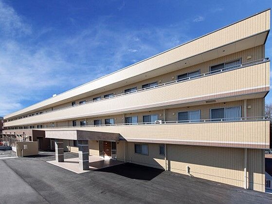 車寄せが付いた玄関があるベージュ系の外壁の３階建ての建物は日当たりのいい場所に建っている。