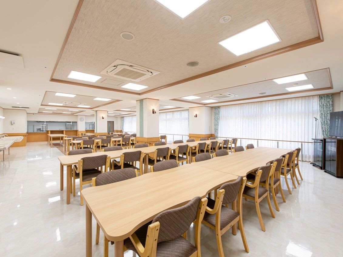 大きなダイニングテーブルセットが複数置かれ、明るい雰囲気の食堂。テレビも設置されている。