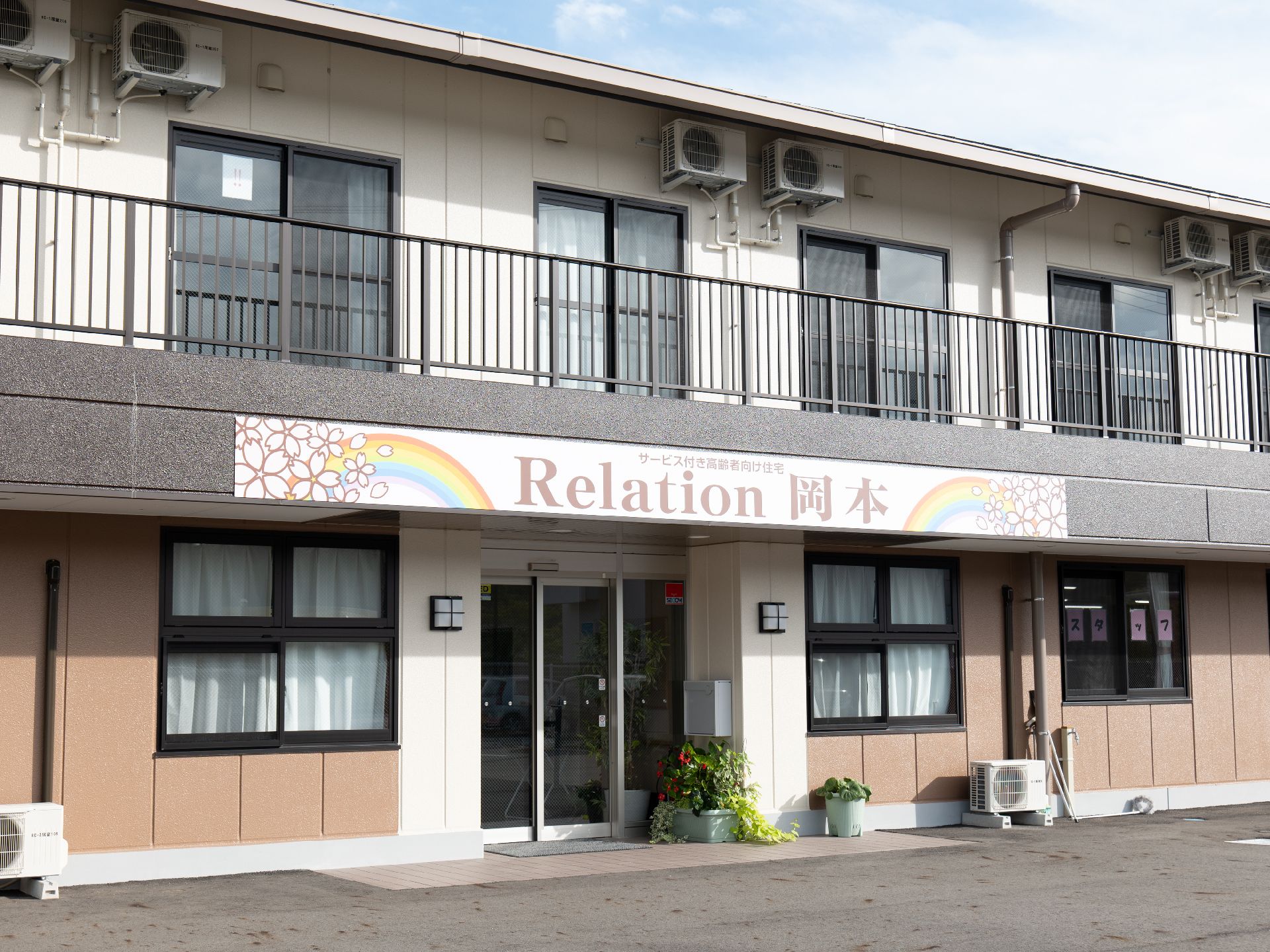 緑の多い屋外で笑顔で過ごしている車いすの高齢女性とエプロンを付けた女性スタッフ。