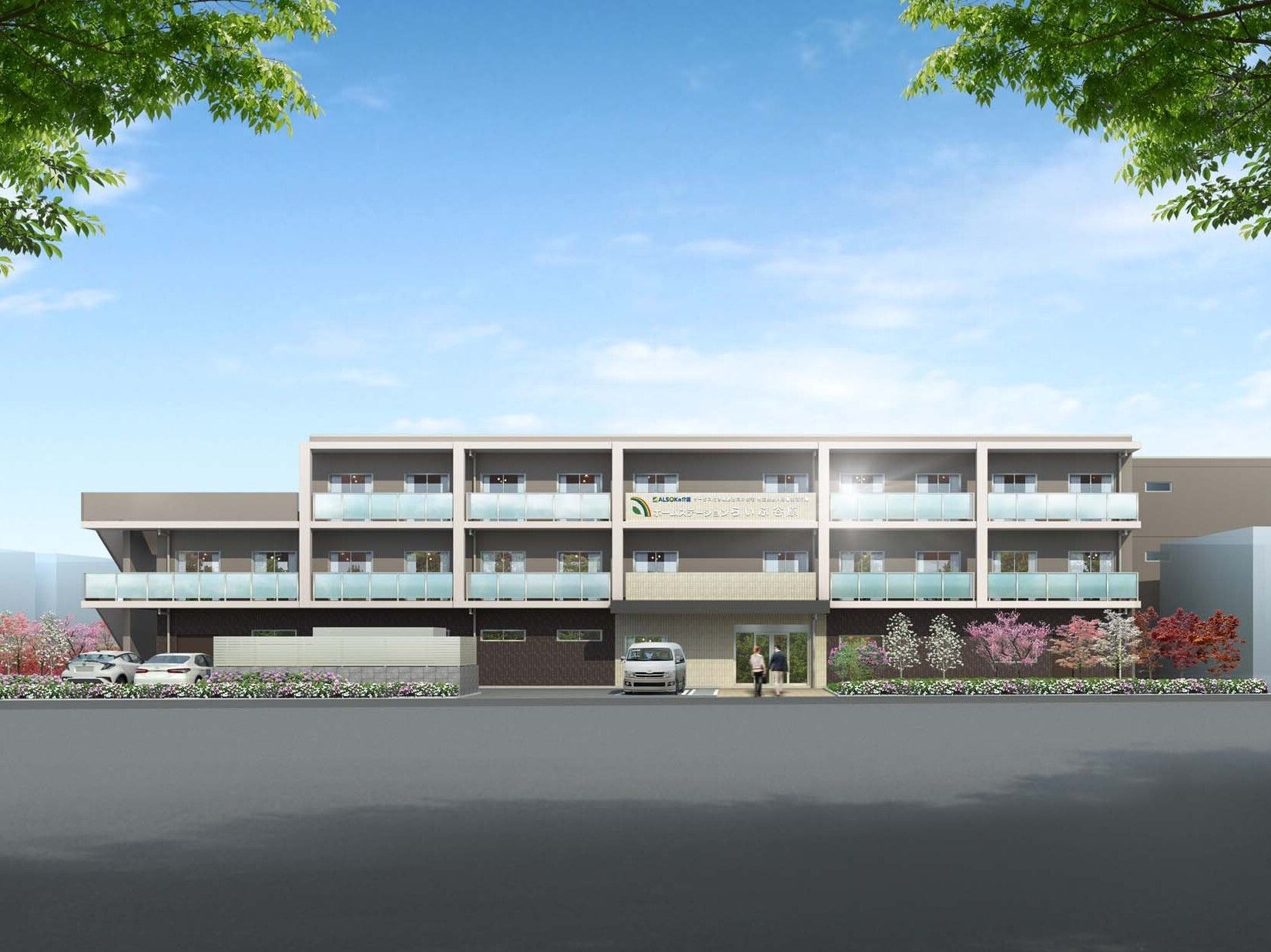 ３階建ての建物はベージュ系で横に長く、各フロアにベランダがあり、草木が植えられている。