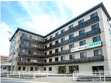 エル字型の建物はベージュとブラウンの外壁で、エル字型。各フロアにベランダが付いている。