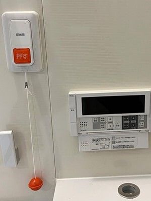 オレンジの呼び出しボタンや操作パネルが設置されたトイレ。操作パネルのふたは開いている。