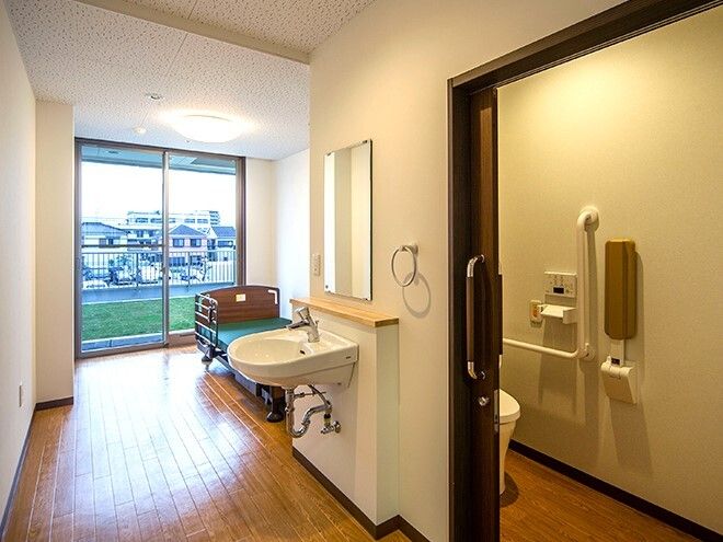 緑の多い屋外で笑顔で過ごしている車いすの高齢女性と付き添いのエプロンを付けた若い女性スタッフ。