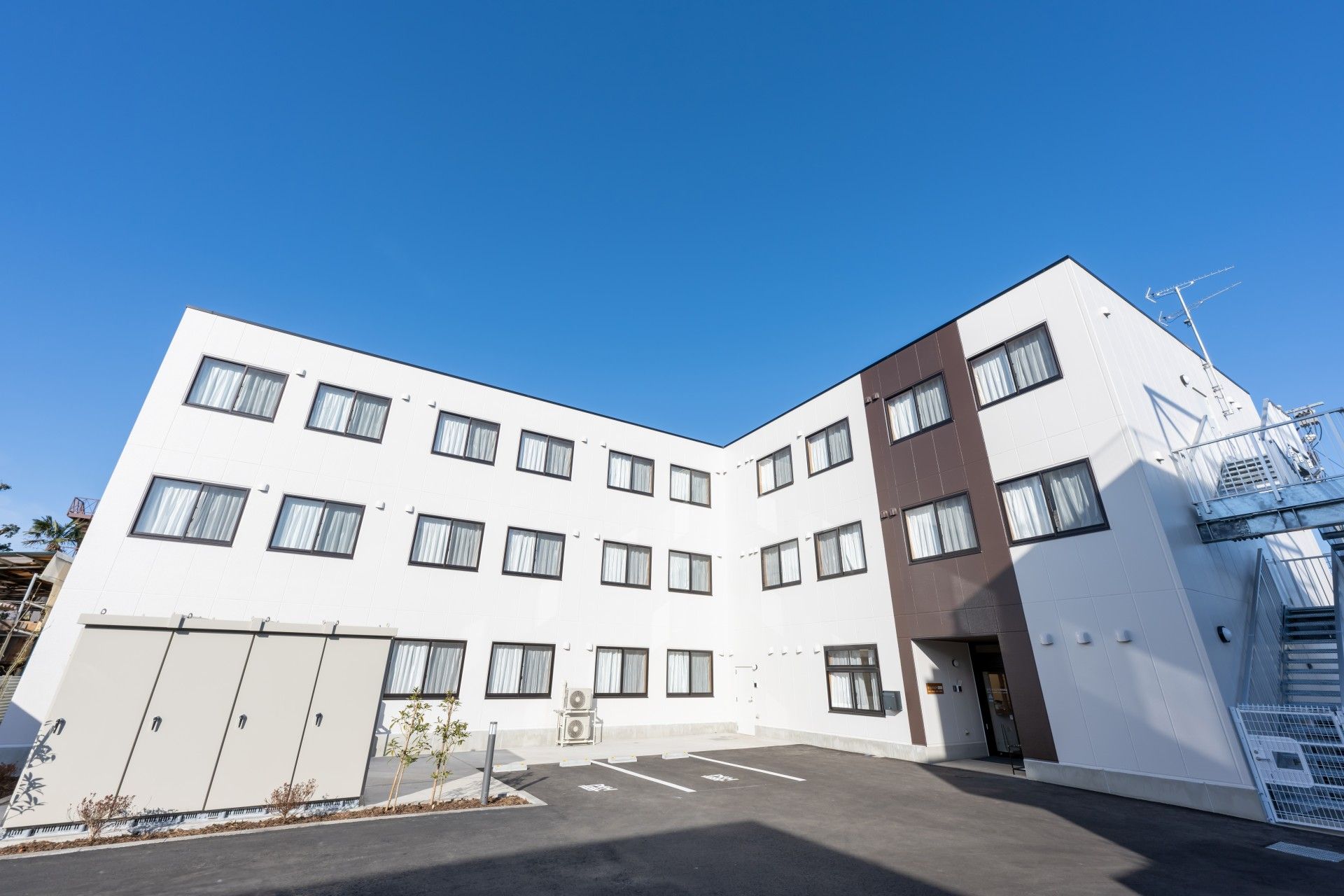 エル字型の３階建ての建物。敷地内には駐車場もあり草木も植えられ、日当たりのいい場所に建っている。