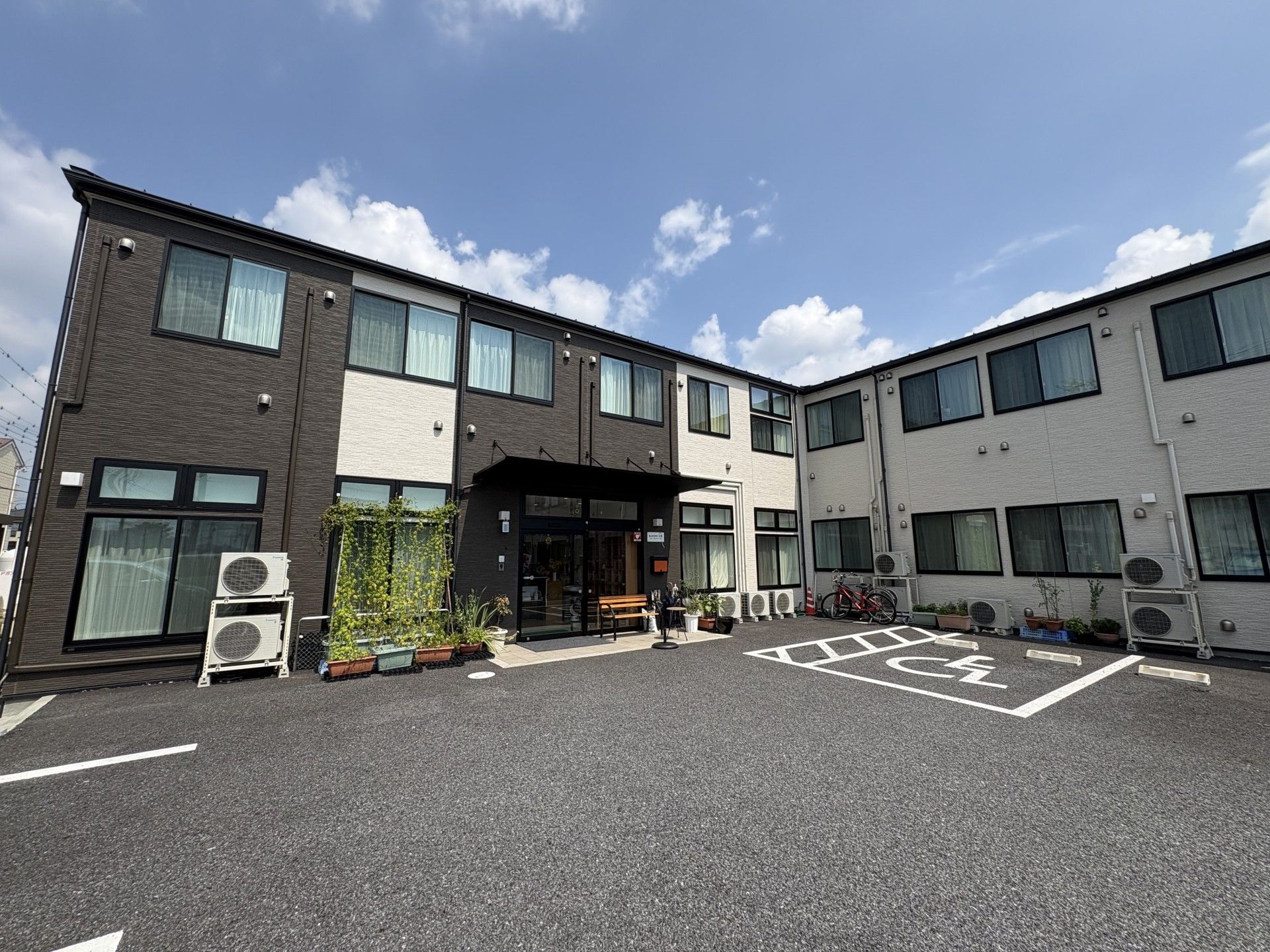 コップを持って微笑んでいるエプロンを付けた女性スタッフ。そばには薬を飲もうとしている高齢女性がいる。