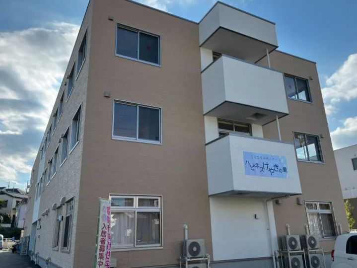 3階建ての建物はブラウン系の外観で角フロアにベランダがあり、周辺には住宅がある。敷地内には駐車場もある。