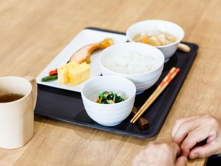 焼き鮭や卵焼き、野菜のグリルが乗った皿がメインで、青菜のお浸し、汁物、白いご飯も盛られている。