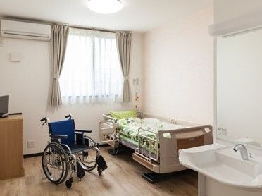 車いす対応の洗面所があるフローリングの部屋には寝具付きのベッドやエアコンがある。