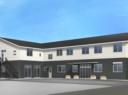 白とダークグレーの２階建ての建物は日当たりのいい場所に建っていて、建物の周りには花が植えられたプランターがある。
