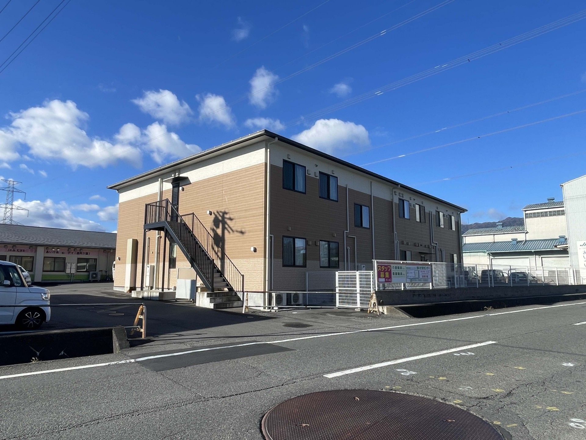 誰かに手を振っている車いすの高齢女性と付き添いのエプロンを付けた女性スタッフ。