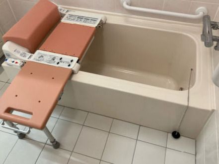 バスリフトが設置された浴槽。座位を保ちやすい浴槽で、浴室内にはタイルが敷かれている。