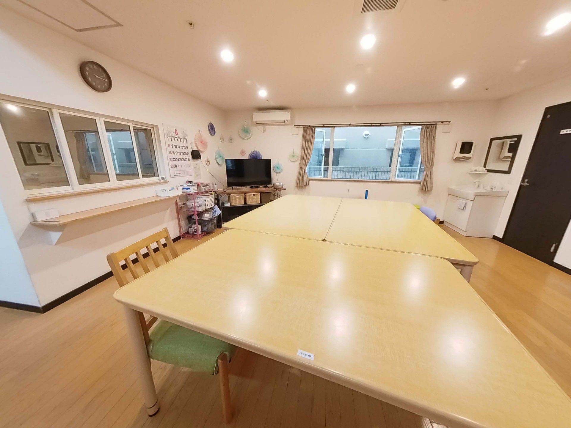 屋外で笑顔で過ごしている車いすの高齢女性。ピンクのエプロンを付けた女性スタッフが車いすを押している。