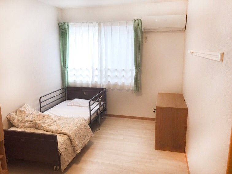 エアコンが付いたフローリングの部屋には寝具付きのベッドやカーテンが付いた窓がある。