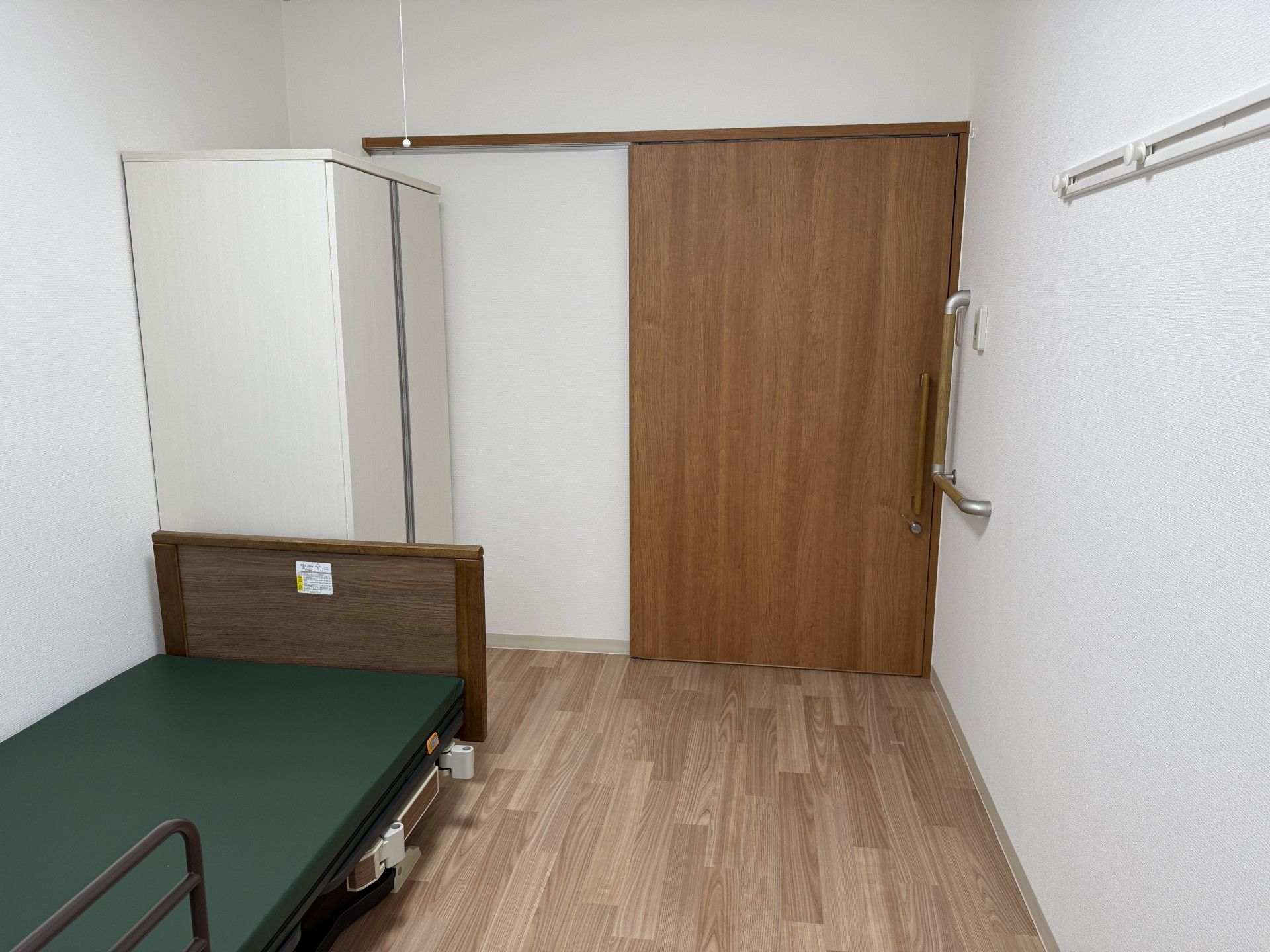 遊歩道のマン内に立ち止まり、笑顔で過ごしている車いすの高齢女性と付き添いのポロシャツを着た女性スタッフ。