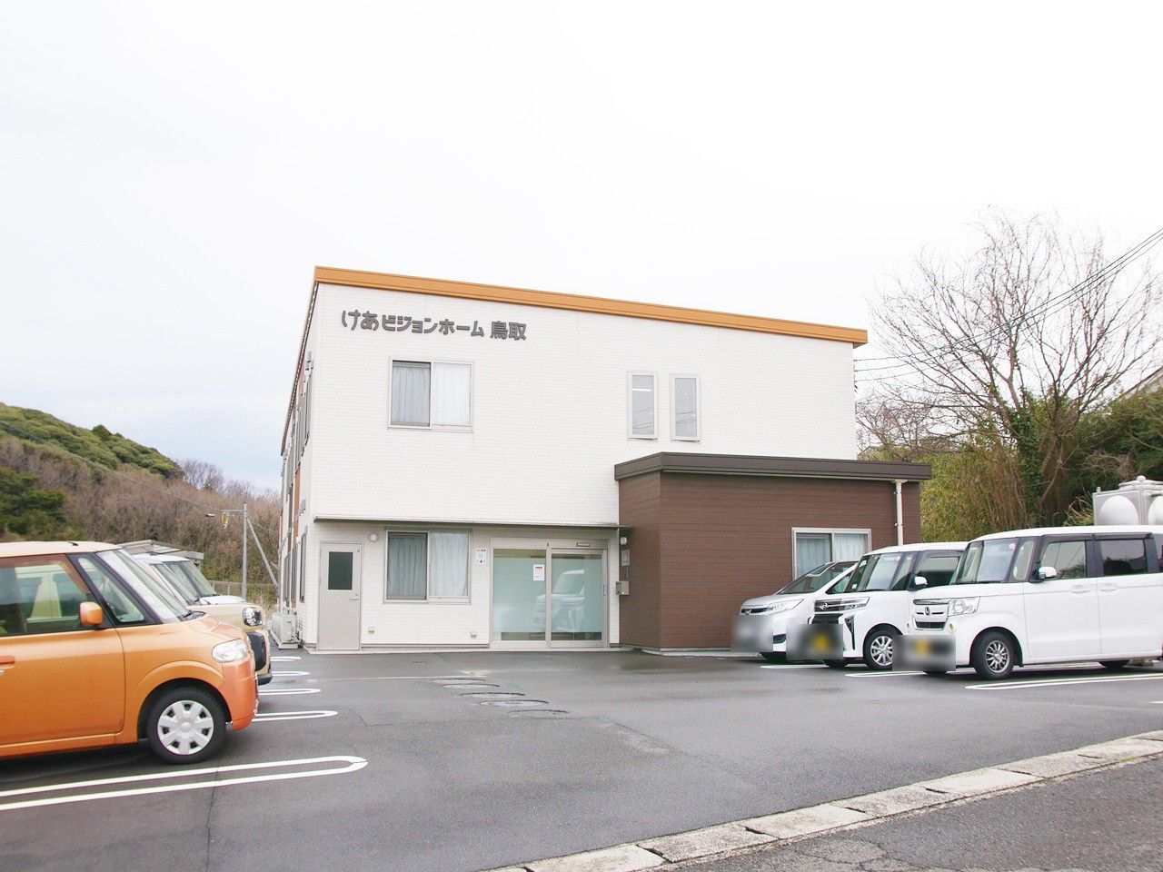 ピンクのエプロンを付けた女性スタッフと車いすの高齢女性が笑顔で話している。