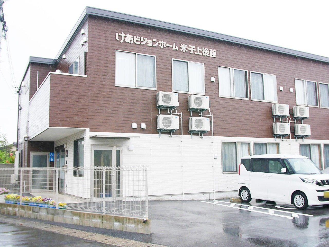 フラワーアレンジメントを楽しんでいる眼鏡をかけた高齢男性。エプロンを付けた若い女性スタッフが手伝っている。